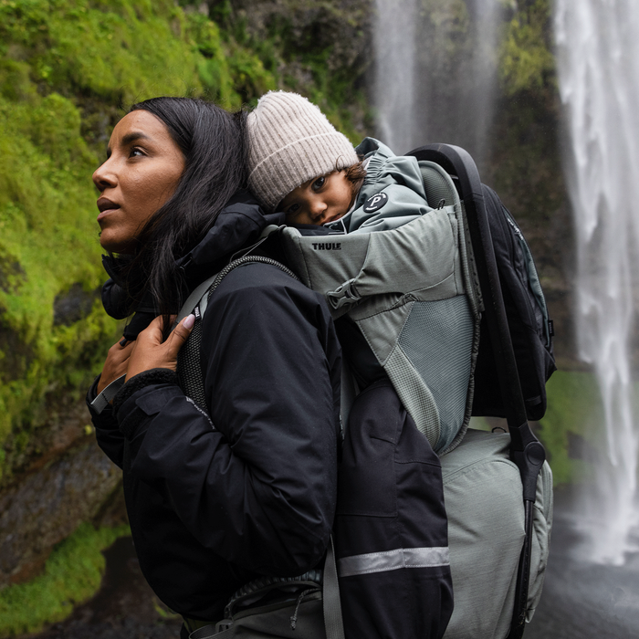 Person carrying a child in a baby carrier with a waterfall in the background