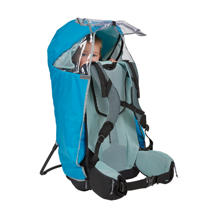 Child in a blue and green backpack carrier with a clear rain cover on a white background
