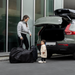 Woman with a child standing next to a car with an open trunk, preparing for a journey with stroller travel bag