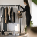 Woman selecting a compactly folded travel bag from a rack of clothes with shoes below.