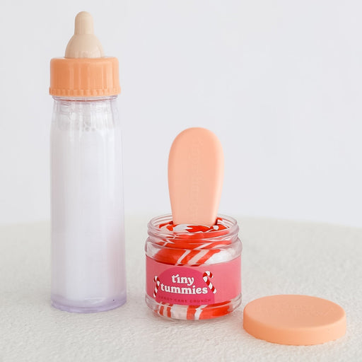 Milk Baby Doll Bottle and festive holiday candy cane coloured jar with 'tiny tummies' branding on a white background