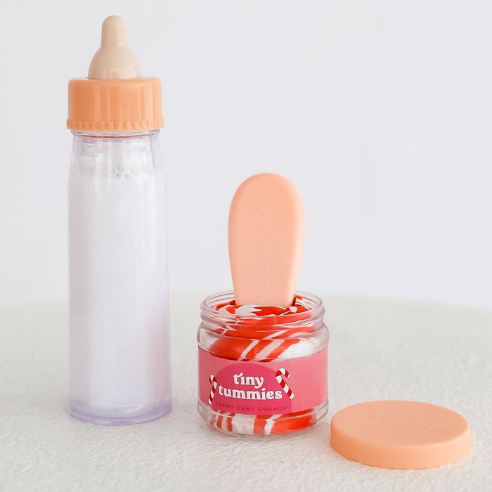 Milk Baby Doll Bottle and festive holiday candy cane coloured jar with 'tiny tummies' branding on a white background