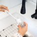 Person using a bottle brush to clean a glass bottle under running water.