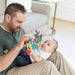Man playing with a baby and a colorful toy in a living room setting.