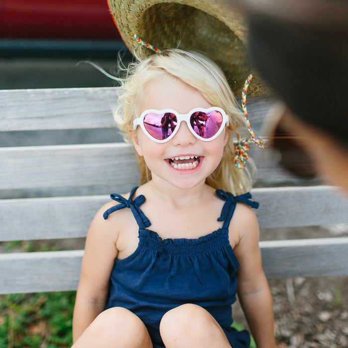 caption-white heart shaped sunglasses on child sitting on park bench