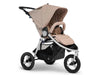 3 wheeled Bumbleride brand stroller with silver frame. Seat is in upright position with canopy extended in soft khaki toned colour called Sand. A padded bumper bar arches over the toddler seat in the same colour fabric. 