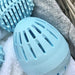 close up of blue shaped egg with pattern of slots in which laundry water can flow through and dirt can be displaced by pellets therfore cleaning and removing dirt.